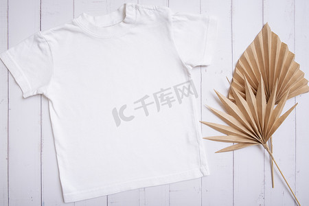 白色儿童 T 恤模型，用于木质背景上的徽标、文字或设计，棕榈叶顶视图