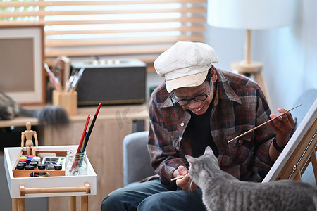 快乐的亚洲男艺术家在家里和他的猫玩耍并画画。