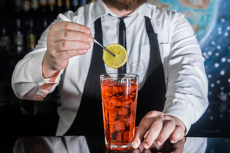 一位专业的酒保在夜总会柜台的玻璃杯中放了一片柠檬和红色冰镇酒精鸡尾酒