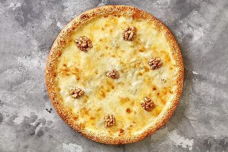 灰色石背景上的奶酪披萨，配有马苏里拉奶酪、帕尔马干酪、埃蒙塔尔奶酪、戈贡佐拉奶酪、核桃和芝麻