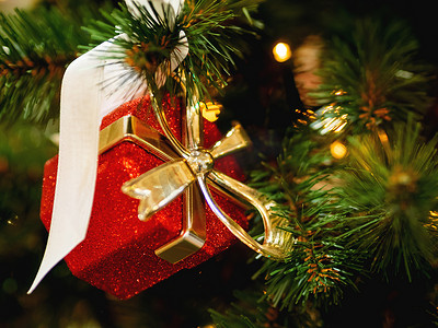 礼物金色丝带摄影照片_新年装饰红色礼物盒，圣诞树上有金色丝带。