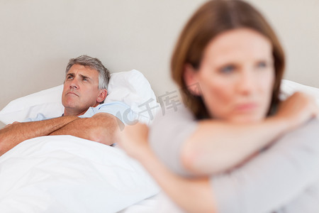 年代感卧室摄影照片_悲伤的男人躺在床上，他的妻子在前景