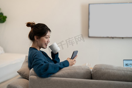 笑脸的亚洲美女坐在客厅的沙发上，在家里度过闲暇时光。