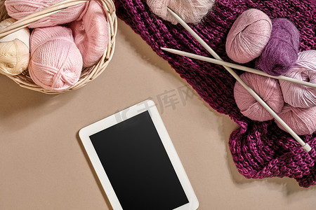 粉红色和紫色的羊毛线球，织针放在米色背景的篮子里。