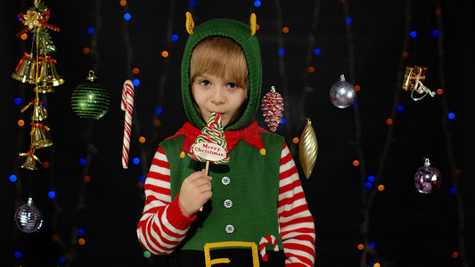 小女孩穿着圣诞精灵圣诞老人助手服装舔着糖果棒棒糖焦糖糖果