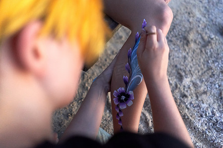 一位艺术家在沙滩上女人腿上画一朵花的俯视图