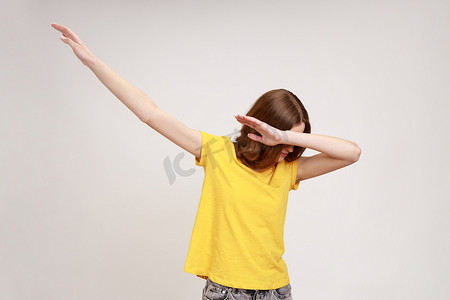 年轻漂亮的女人的肖像，棕色波浪发，穿着黄色休闲 T 恤，做出流行的轻拍舞蹈手势，互联网趋势。