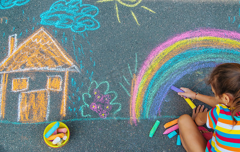 孩子用粉笔在柏油路上画了一栋房子和一条彩虹。