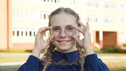 戴眼镜的青少年人摄影照片_一名戴眼镜的少女在学校门前。