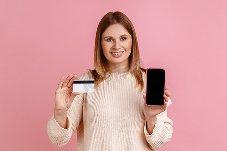 微笑乐观的女人拿着信用卡和黑屏手机，网上银行。