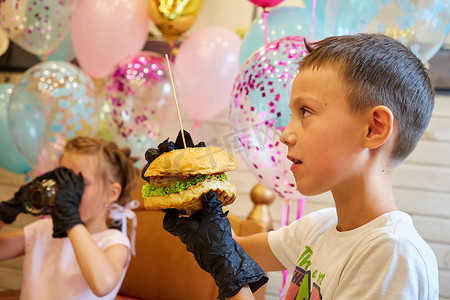英俊的小男孩戴着黑色橡胶手套吃汉堡。