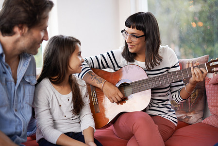 坐弹吉他摄影照片_一个一起玩耍的家庭……一个女人和家人坐在一起弹吉他。