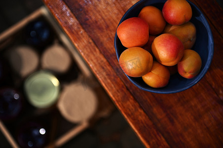 专注于木桌上陶瓷碗中成熟的即食杏子，与地板上放着果酱罐的模糊盒子相对