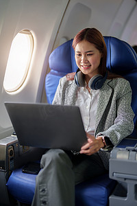 飞机上一位身着正装的成功亚洲女商人或女企业家坐在商务舱座位上，在飞行期间使用笔记本电脑