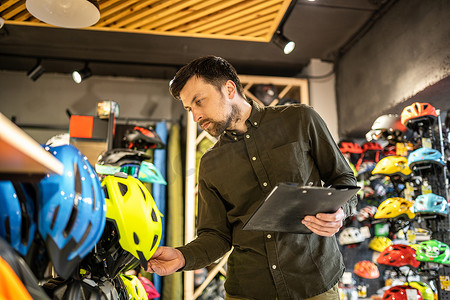信息查看摄影照片_自行车店经理在平板电脑上查看头盔价格信息，卖家在体育用品店盘点。