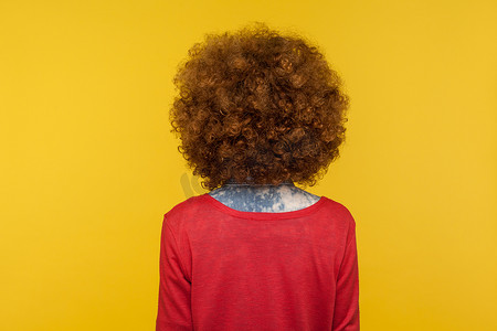 卷发背面摄影照片_黄色背景上情感卷发女孩的背面肖像。