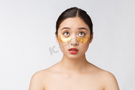 亚洲美女少女用金色眼罩贴在眼睛下方，忧心忡忡地护理皮肤。