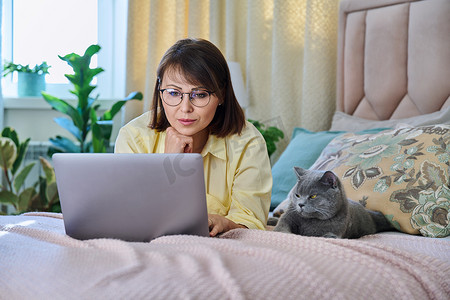 中年妇女在家里用笔记本电脑和宠物猫在床上放松