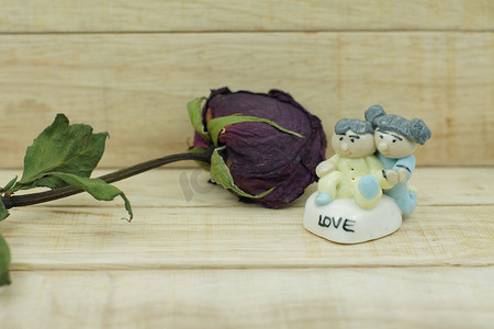 瓷娃娃摄影照片_木纹背景上的干玫瑰和陶瓷娃娃