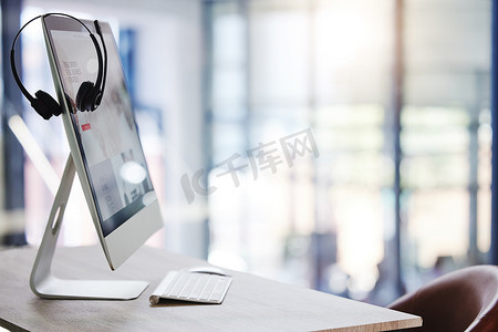 在空荡荡的呼叫中心办公室的电脑桌面显示器上挂着耳机的特写镜头。