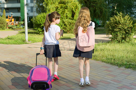 两个女学生女朋友小学生在院子里背着书包走路的后视图
