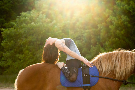 在树木的背景下骑马做瑜伽的年轻女子