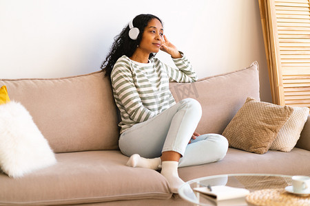 非裔美国女性在客厅的沙发上放松时一边用耳机听有声读物