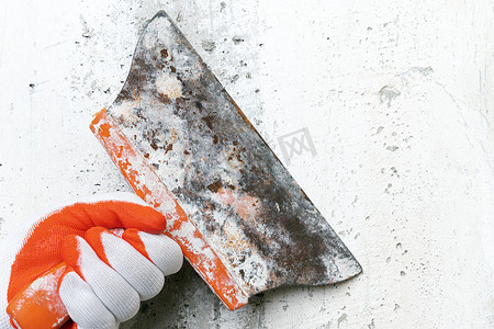 泥水匠的手拿着一把旧油灰刀刮混凝土内墙，去除旧石膏