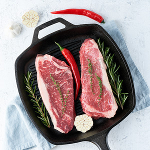 铸铁大锅中的两块新鲜生大整块肉、牛肉片、大理石西冷牛排