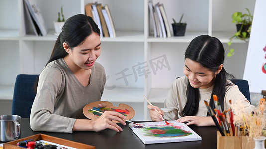 有爱心的老师在美术课上帮助小女孩画画。