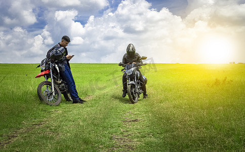 道路故障摄影照片_两个男人骑着摩托车停在田野里聊天，两个年轻的摩托车手在田野里，两个骑着摩托车的男人在美丽的乡村道路上，年轻的摩托车手停在路上