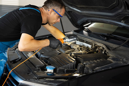 身穿蓝色制服的白人男性机械师在带灯的汽车服务中检查电机。