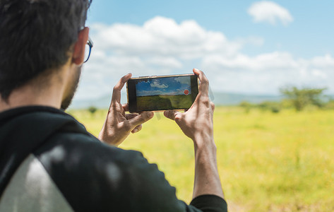 一个人用手机在田野里拍照的后视图，一个男人在田野里拍照的后视图，游客特写镜头在风景中拍照。