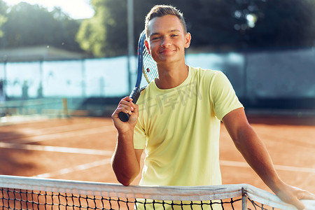 在红土场上，拿着网球拍站在网边的青年少年
