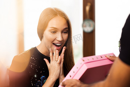惊讶的年轻女子打开了一个粉红色的盒子，里面装着礼物。