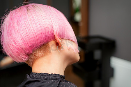 在美发沙龙里为年轻模特的后视图设计和剪裁染成粉红色的头发。