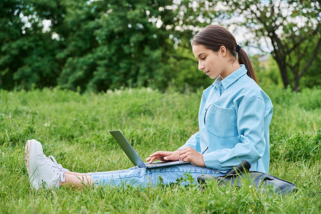 十几岁的女高中生坐在绿草上使用笔记本电脑
