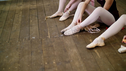 特写，芭蕾舞演员在旧木地板上，在芭蕾课上把鞋子换成特殊的芭蕾舞鞋、足尖鞋、带芭蕾丝带的蕾丝。