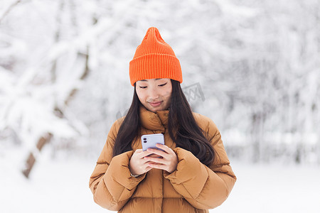 冬天下雪的时候，美丽的亚洲女人在公园里散步，用手机网上购物