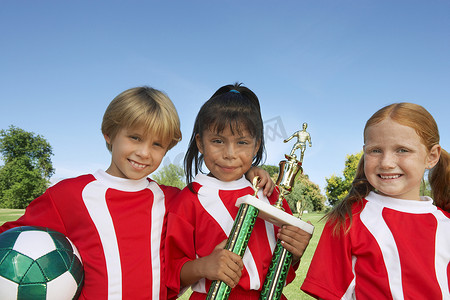 儿童足球队在球场上拿着球和奖杯的肖像