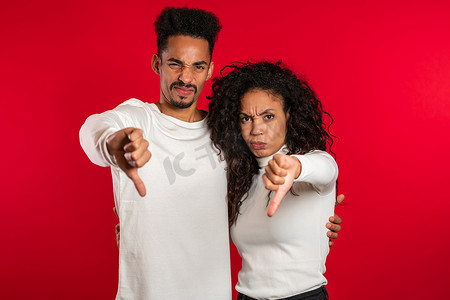年轻的非洲夫妇站在红色工作室背景上表达不满，并对着镜头表现出拇指向下的手势。