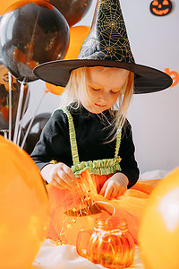 儿童万圣节-一个戴着女巫帽的女孩和一个狂欢节服装，家里有通风的橙色和黑色气球。