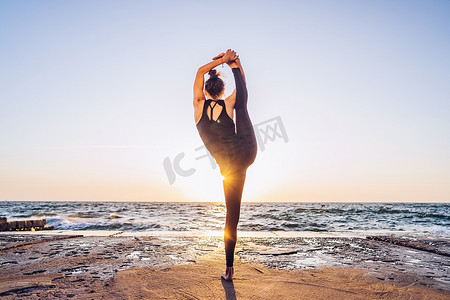穿着黑色紧身衣裤的苗条女人在日出时在海边或海洋附近练习瑜伽。