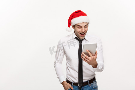 圣诞节概念-英俊的商人戴着圣诞老人的帽子玩平板电脑，面部表情令人惊讶。
