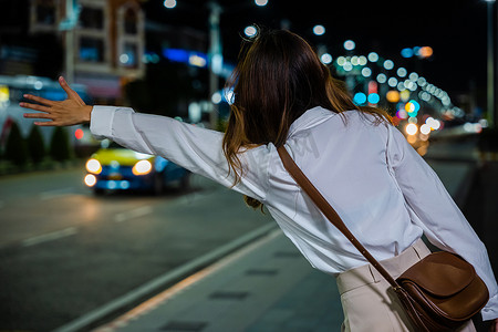 行走在路上摄影照片_晚上，在繁忙的城市街道上，女商人站在路上挥舞着出租车