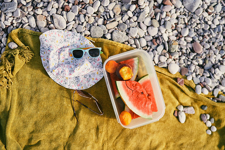 海滩上毯子上放着西瓜和桃子的塑料盒