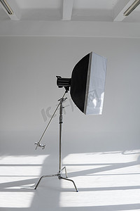 专业照片闪光灯，在带有巨大窗户的现代摄影工作室的天幕上的 C 形支架上配有一个大柔光箱。