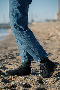 穿着牛仔裤和绿色袜子的男人的腿在沙滩上的沙滩上。