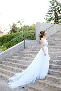 欧洲新娘走在混凝土楼梯上，穿着白色连衣裙的背影。