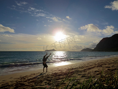 一名男子穿着 T 恤和短裤在欧胡岛 Waimanalo 海滩上倒立